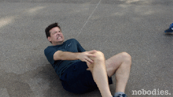 Man lying on the floor in pain and holding his knee gif
